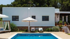 A modern house with a swimming pool, two lounge chairs, and a pergola with an umbrella. - New! Villa Can Curreu III - Santa Gertrudis (Ibiza)