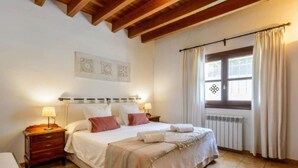 A bedroom with a bed, two bedside tables with lamps, a radiator, and a window with curtains. - New! Villa Can Curreu III - Santa Gertrudis (Ibiza)