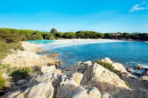 A coastal landscape with rocky terrain, a sandy beach, and a clear blue sea.