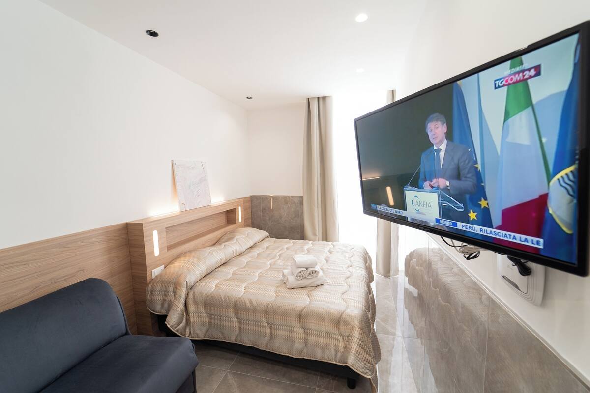 Une chambre d’hôtel équipée d’un lit, d’un canapé, d’un téléviseur diffusant un programme d’information et d’un autre téléviseur fixé au mur.
