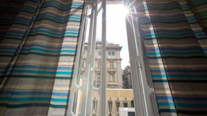 Blick durch ein Fenster mit gestreifter Vorhang, der ein mehrstöckiges Gebäude mit Balkonen zeigt.