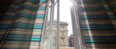 Une vue à travers une fenêtre ornée de rideaux à rayures, dévoilant un immeuble à étages multiples et doté de balcons.