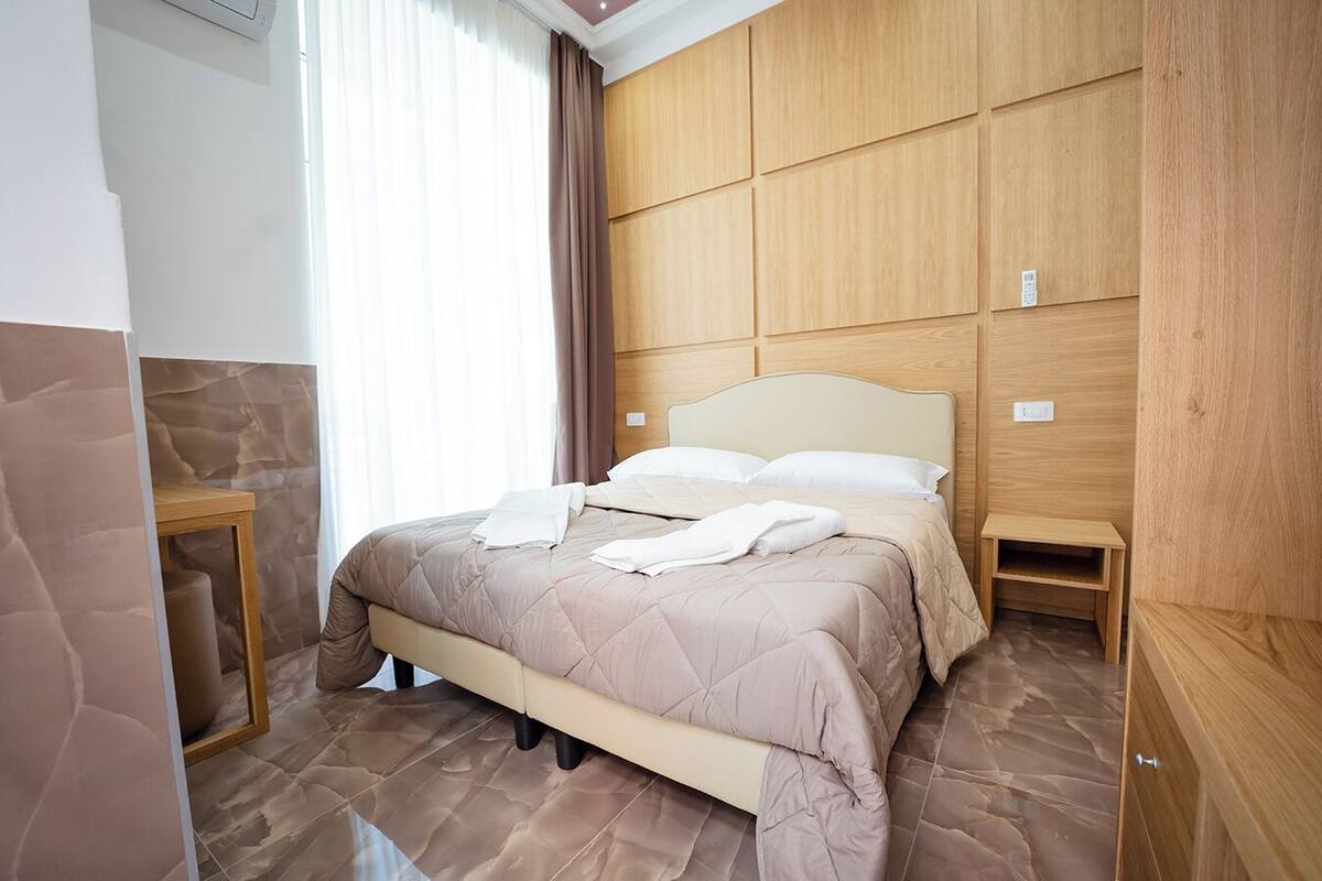Une chambre bien rangée, avec un lit, des tables de chevet et un mur recouvert de panneaux en bois.