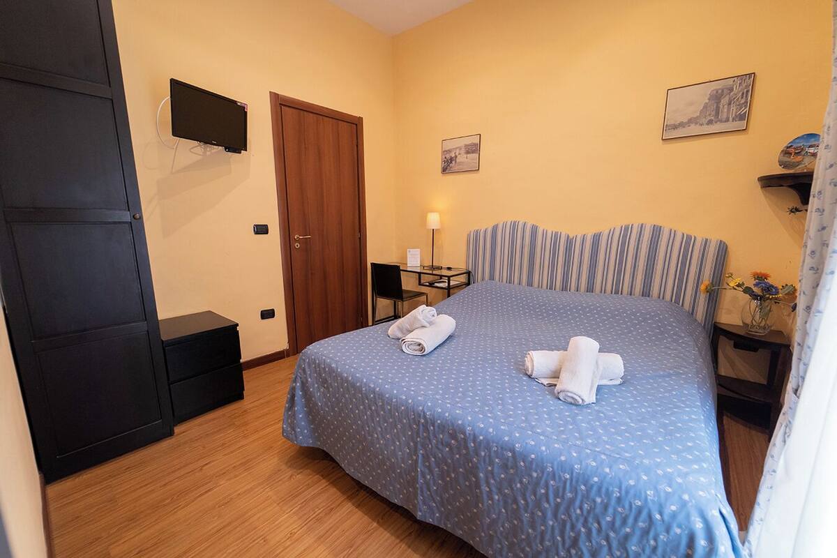 Une chambre d’hôtel avec un lit, un bureau, une chaise, une télévision et une porte.
