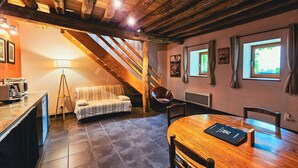 A cozy room with a wooden ceiling, a sofa, a dining table with chairs, a lamp, and a window with curtains. - Family-Friendly 1BR w/ Garden View + Hot Tub (Étivey)