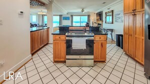 A kitchen with wooden cabinets, a central island, and a view of the ocean. - Oceanside Manor – Your Big, Pet-Friendly Retreat (Surf City)