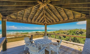 Un espace extérieur abrité, doté d’une table et de chaises en bois, avec vue sur une plage.