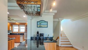 A kitchen with wooden cabinets, a black countertop, a coffee maker, and a sign that reads 'Our Beach House.' - Oceanside Manor – Your Big, Pet-Friendly Retreat (Surf City)