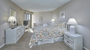 A bedroom with a bed, two bedside tables, a dresser, a television, and a chair. - Atlantis 704-2BR/2BA Myrtle Beach-Walk to Beach (Myrtle Beach)