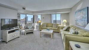 A living room with a television, two sofas, a coffee table, and a large window with a city view. - Atlantis 704-2BR/2BA Myrtle Beach-Walk to Beach (Myrtle Beach)