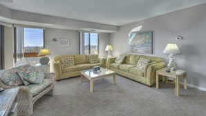 A living room with a sofa set, two side tables with lamps, and a view through large windows. - Atlantis 704-2BR/2BA Myrtle Beach-Walk to Beach (Myrtle Beach)