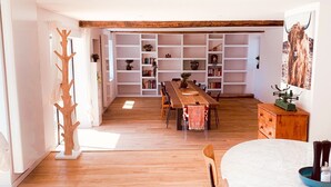 Un grand espace dédié à la salle à manger, avec une longue table en bois et des chaises, un mur blanc orné d’une bibliothèque et un porte-manteau en bois.