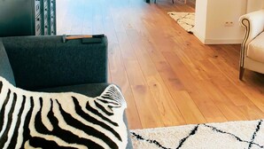 Un vaste espace de vie doté d’un plancher en bois, d’un canapé, d’une table à manger avec des chaises, et offrant une vue sur une voiture garée et sur la verdure environnante.