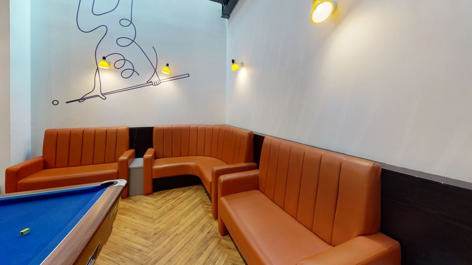 A pool table with orange cushioned seating and a wall mural.