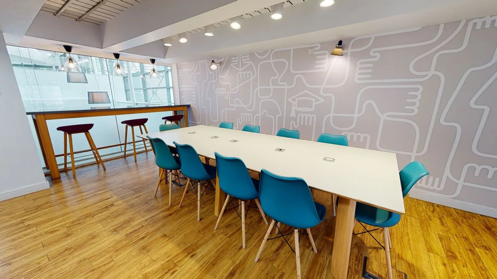 Une salle de conférence dotée d’une longue table et de chaises bleues, d’un parquet en bois et d’un décor mural moderne.