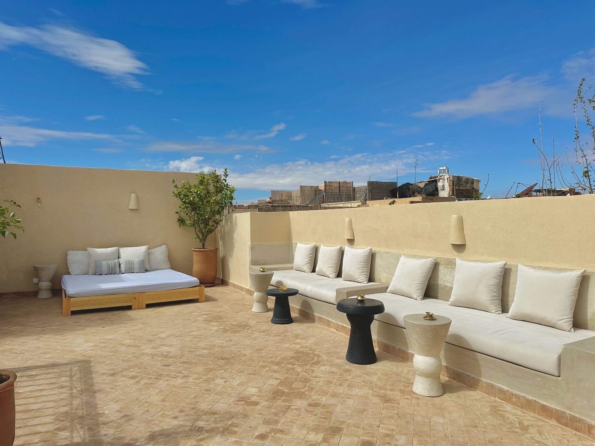 Eine Dachterrasse mit einer beigen Wand, einer Couch, einem Bett und einem Topfpflanzen.
