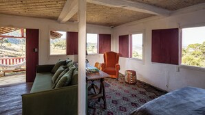 Ein Zimmer mit einem grünen Sofa, einem orangefarbenen Sessel, einem kleinen runden Tisch und einem gemusterten Teppich.