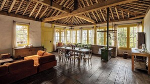 Ein rustikaler Raum mit hoher Holzbalkendecke, einem Holztisch mit Stühlen, einer Couch und einem Fenster mit Vorhängen.