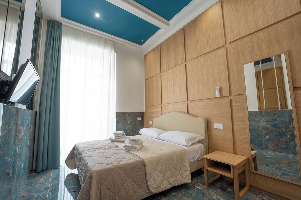 A hotel room with a bed, a bedside table, a mirror, and a wall-mounted TV.