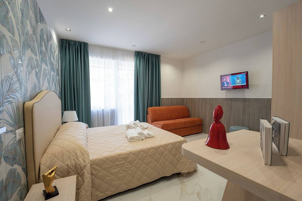 A hotel room with a bed, a desk, a chair, a television, and a decorative statue.