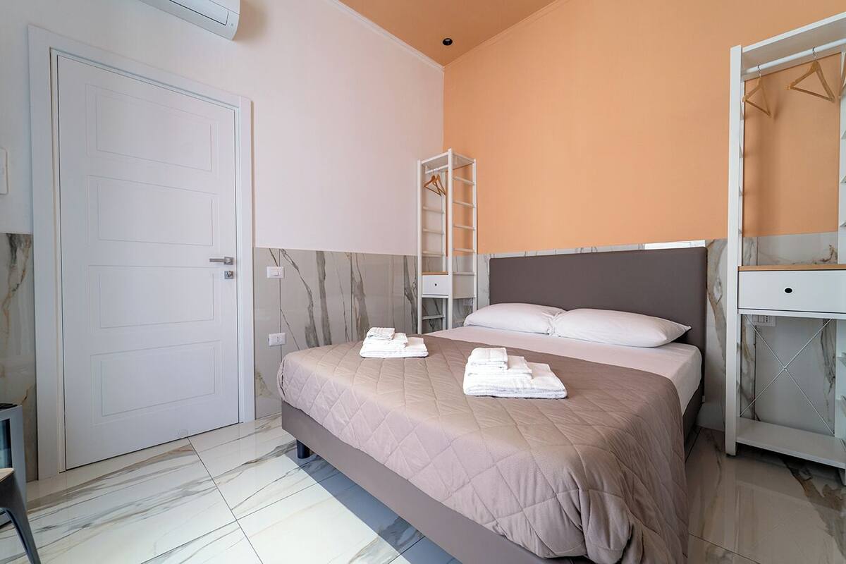 A neatly arranged bedroom with a bed, a wardrobe, and a shelf unit.