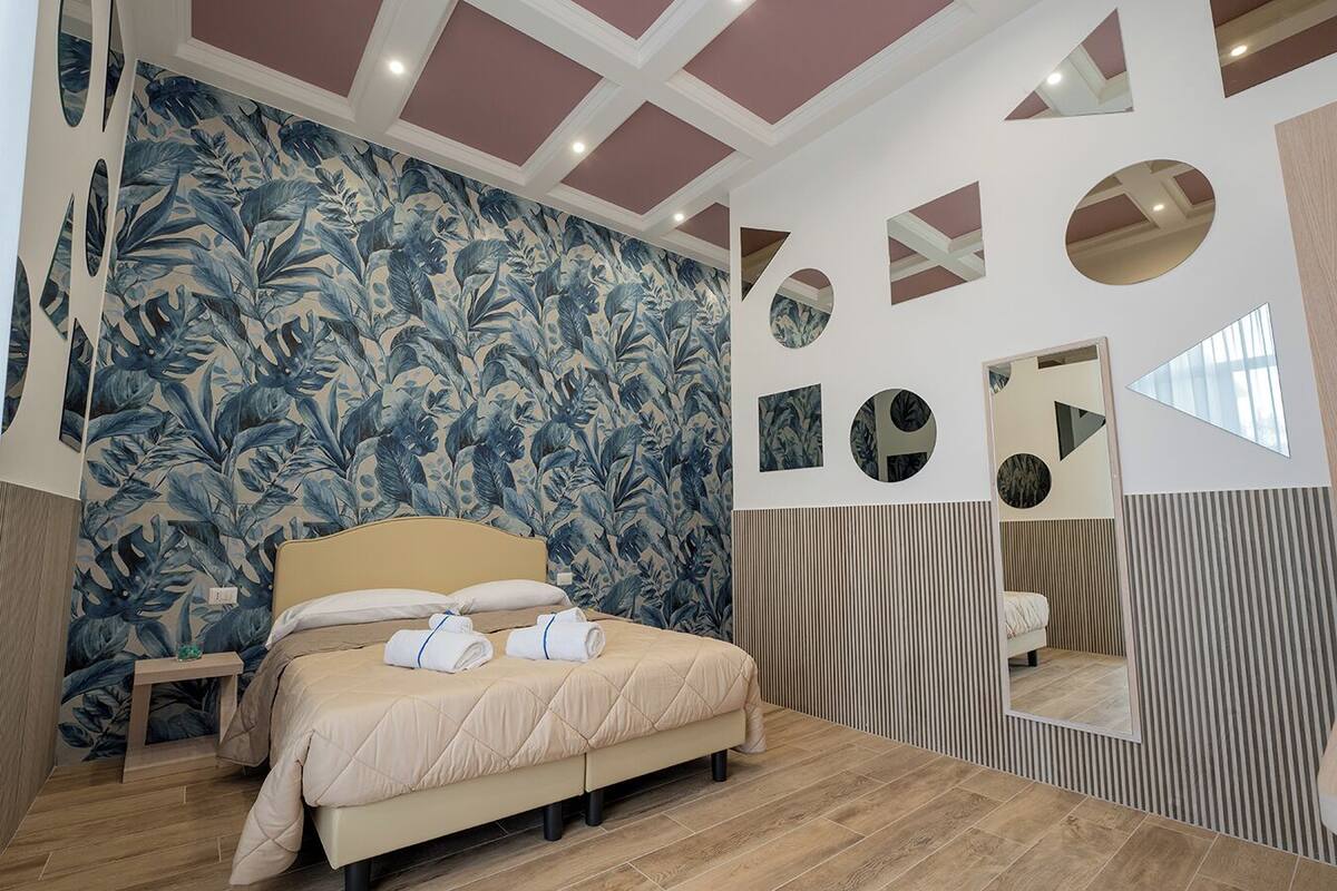 A bedroom with a bed, a nightstand, a mirror, and a wall with a tropical leaf pattern.
