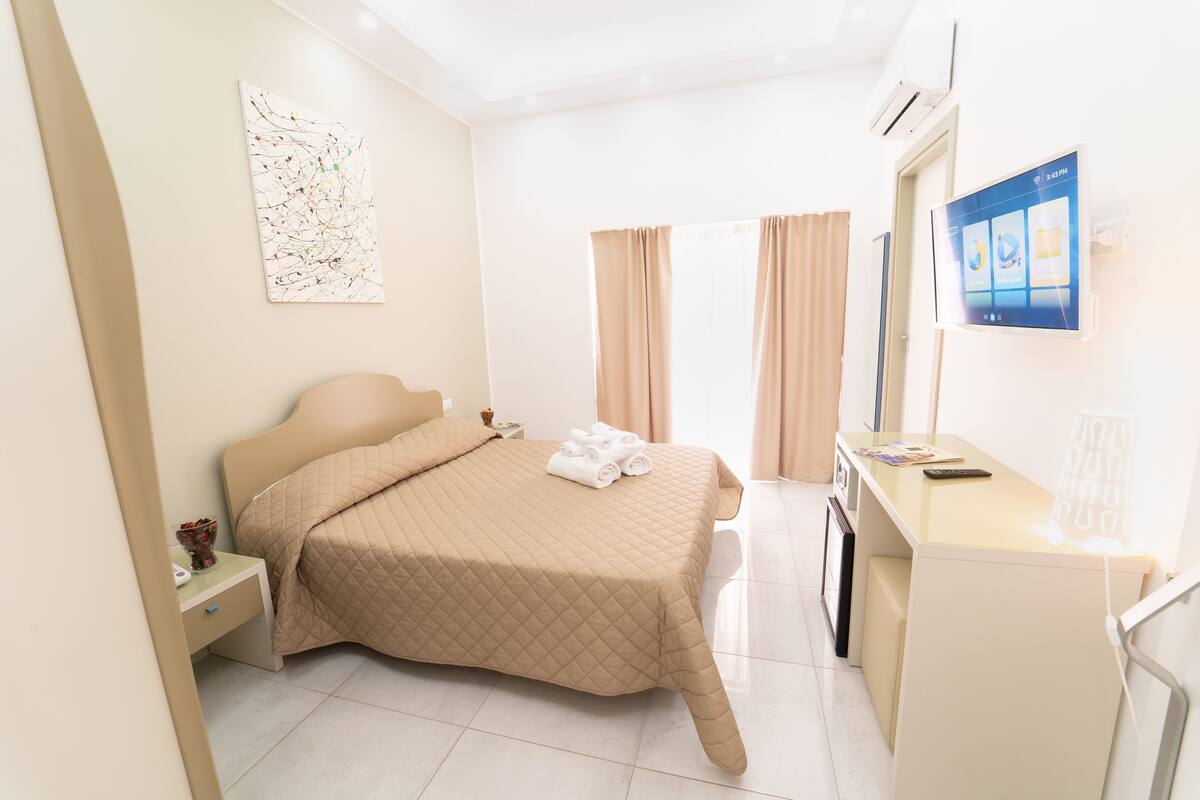 A hotel room with a bed, a desk, a TV, and a window with curtains.