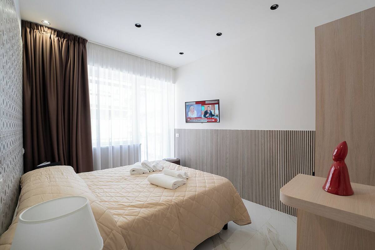 A modern hotel room with a bed, a desk, and a TV mounted on the wall.