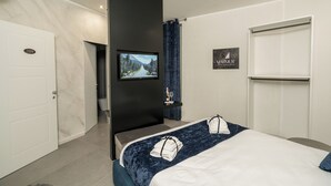 Quarto de hotel moderno com parede de mármore, uma cama grande com colcha azul, televisão de tela plana e uma placa com a inscrição "ARMUR".