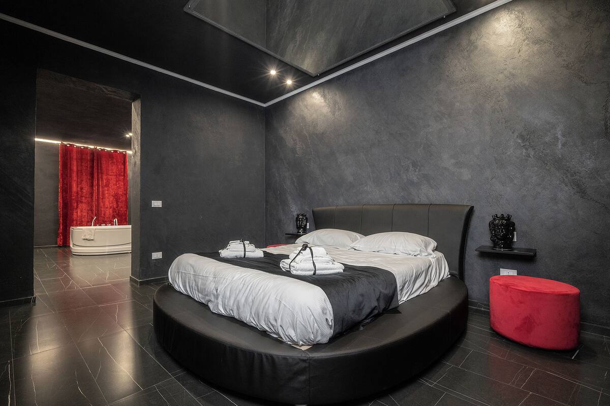 A modern bedroom with a curved bed, a red ottoman, and a built-in bathtub.