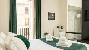 Quarto de hotel moderno com uma cama grande, uma pequena escrivaninha, área de chuveiro e vista para o exterior.