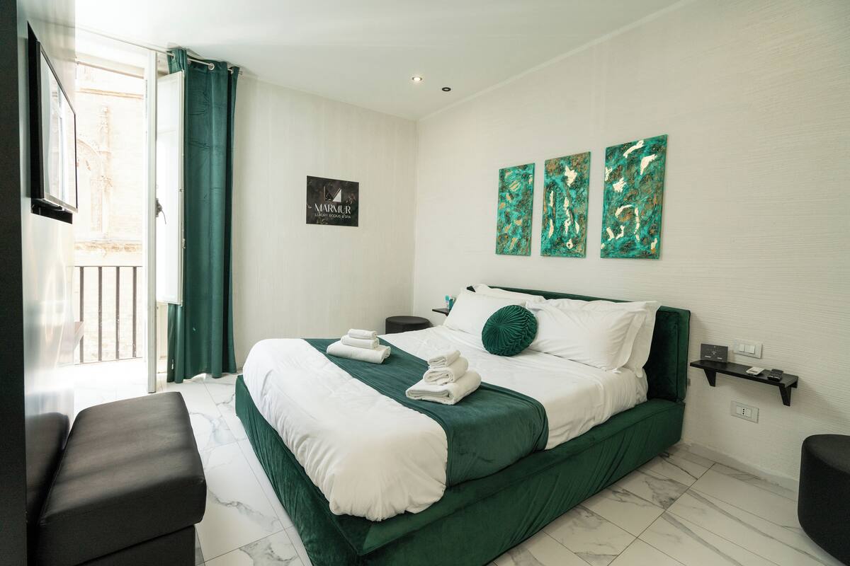 A hotel room with a bed, a bench, a nightstand, and a wall-mounted shelf.