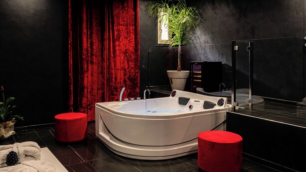 Casa de banho moderna com uma banheira grande, detalhes em vermelho e uma planta em vaso.