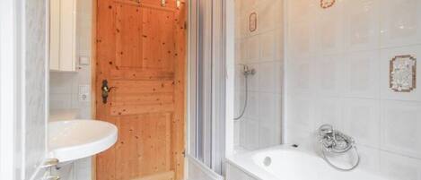 Un baño con puerta de madera, lavamanos blanco, ducha y bañera.