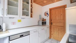 A compact kitchen with white cabinets, a microwave, and a wooden door. - Vacation apartment - Klenk - 1 (Gruibingen)