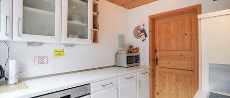 A compact kitchen with white cabinets, a microwave, and a wooden door.