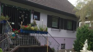 A two-story house with a sloped roof, a small balcony, and a front yard with a lawn and a birdbath. - Vacation apartment - Klenk - 1 (Gruibingen)