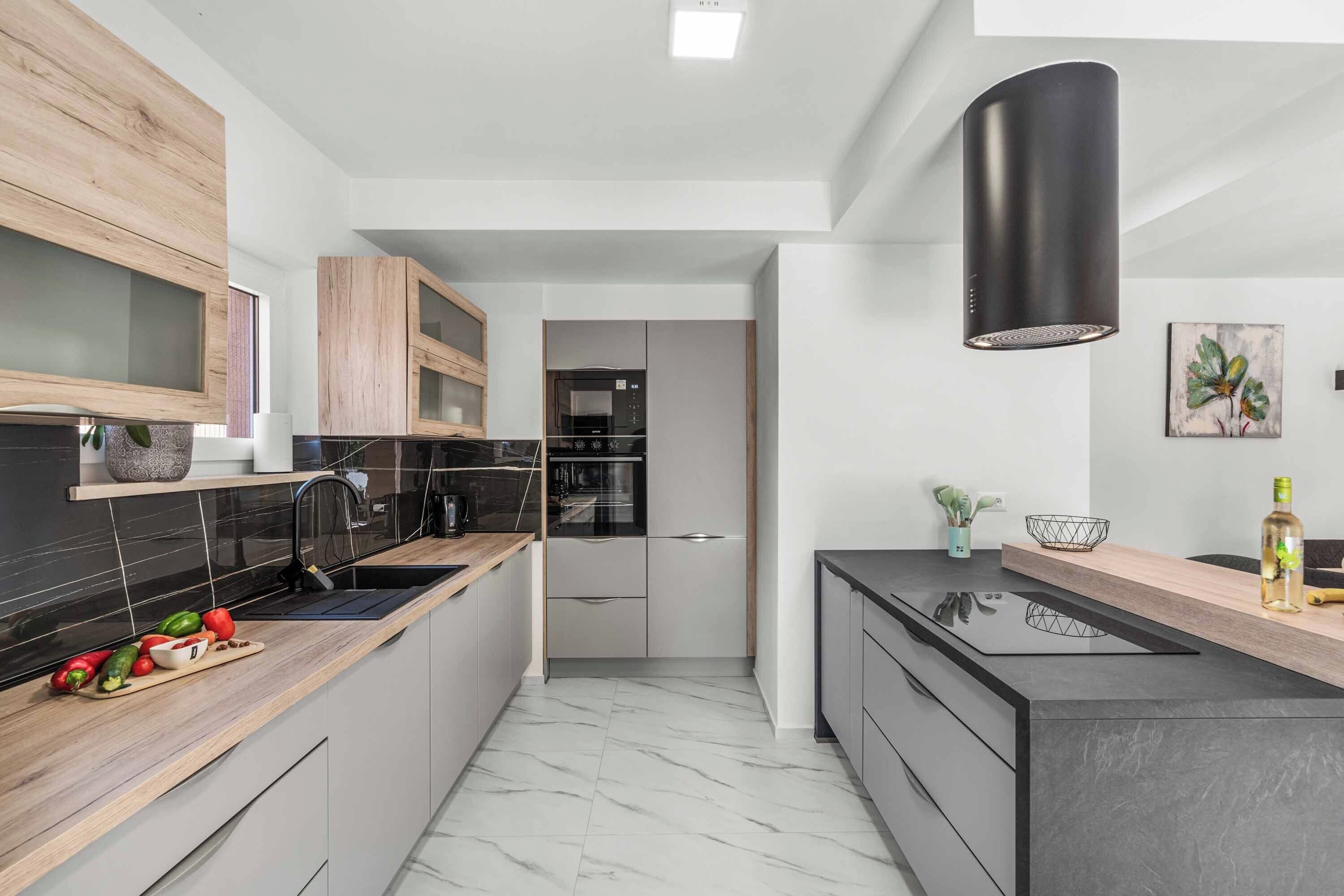 A modern kitchen with wooden cabinets, a black countertop, and a stainless steel range hood.