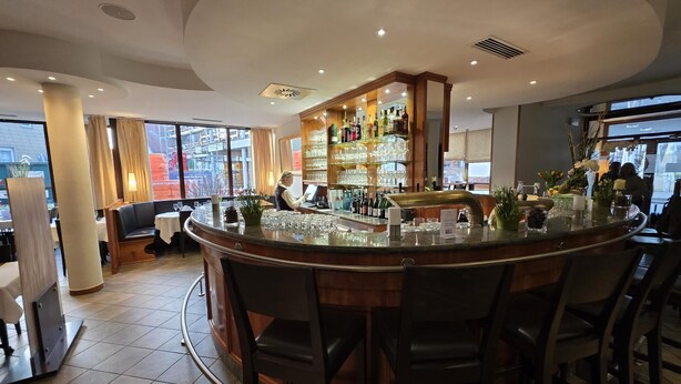 Zona de bar moderna con mostrador curvo, taburetes y estantería bien surtida con botellas y copas.