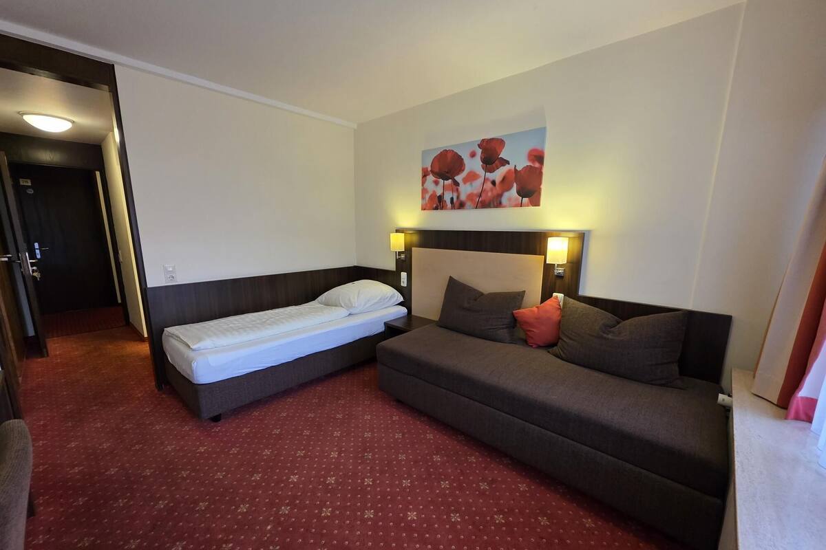 A hotel room with a bed, a sofa, and a wall-mounted artwork.