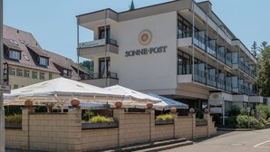 Un hotel moderno con un letrero llamativo que dice "SONNE-POST". Cuenta con un edificio de varios pisos con balcones y ventanas grandes.