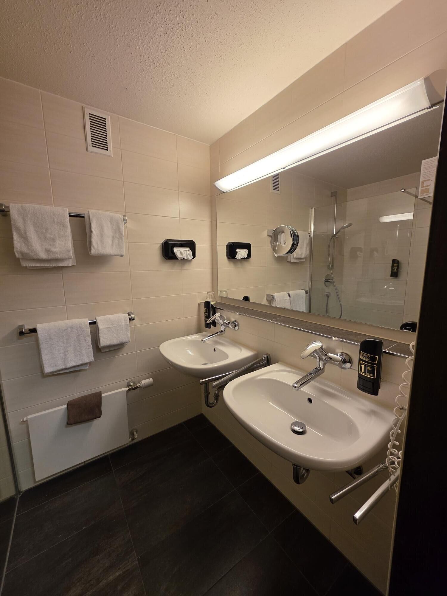 A modern bathroom with two sinks, a large mirror, and towel racks.