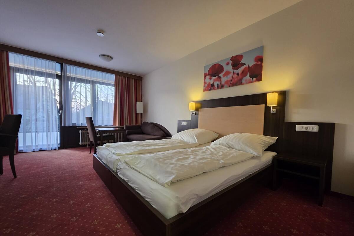 A hotel room with a large bed, a desk, a chair, and a window with curtains.