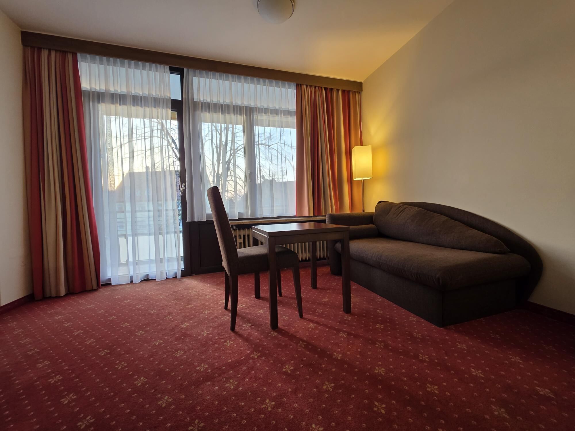 Ett hotellrum med en röd matta, en soffa, en fåtölj, ett bord och en lampa.