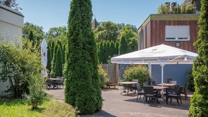 Un patio al aire libre con mesas y sillas, rodeado de vegetación y un edificio con un letrero.