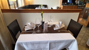 Mesa de comedor dispuesta para cuatro personas, con manteles blancos, copas de vino y un atril para el menú.