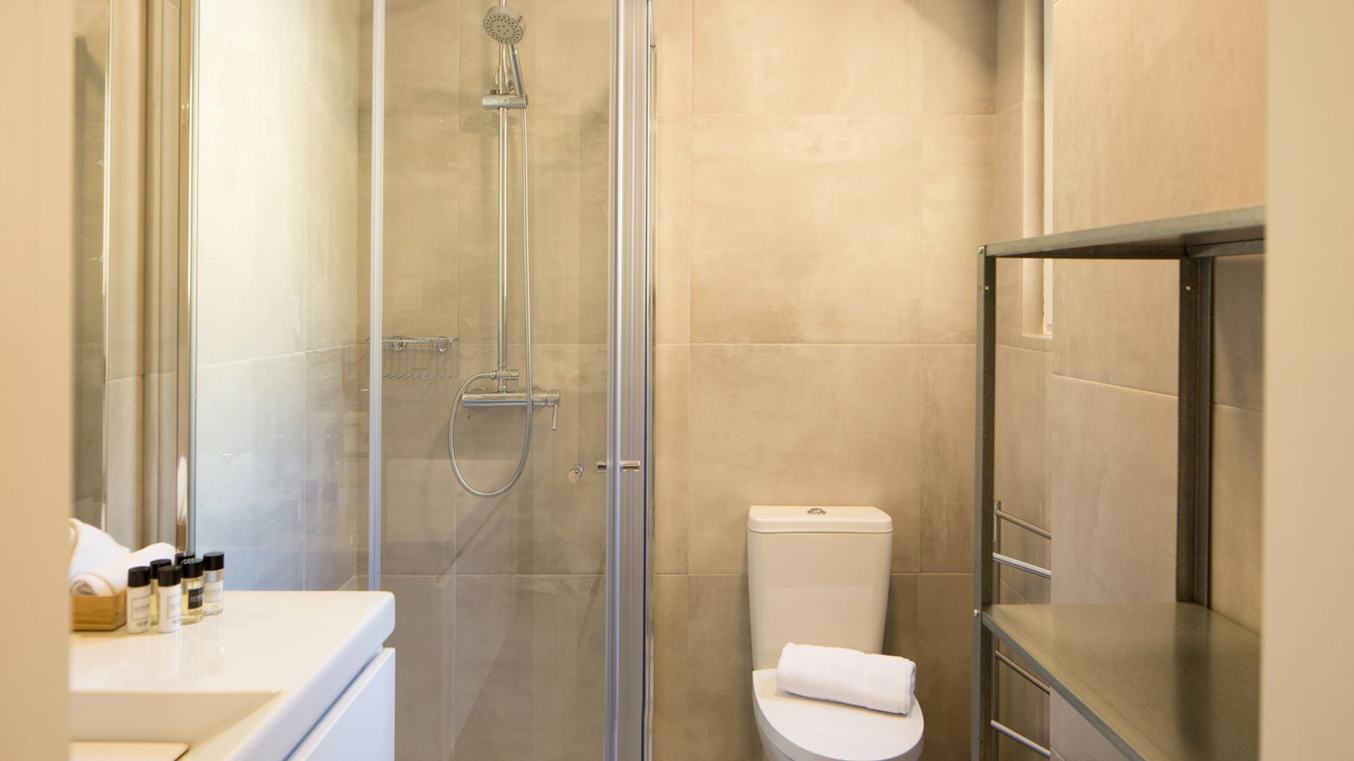 Et moderne badeværelse med et glasafskærmet brusebad, toilet og et vaskemøbel med toiletartikler.