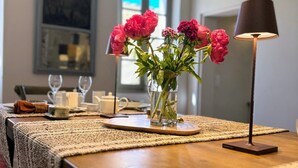 Una mesa de comedor con un mantel tejido, un florero con flores rosas y una lámpara.