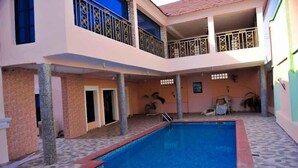 Um edifício de dois andares com piscina, varandas e chão de azulejos.