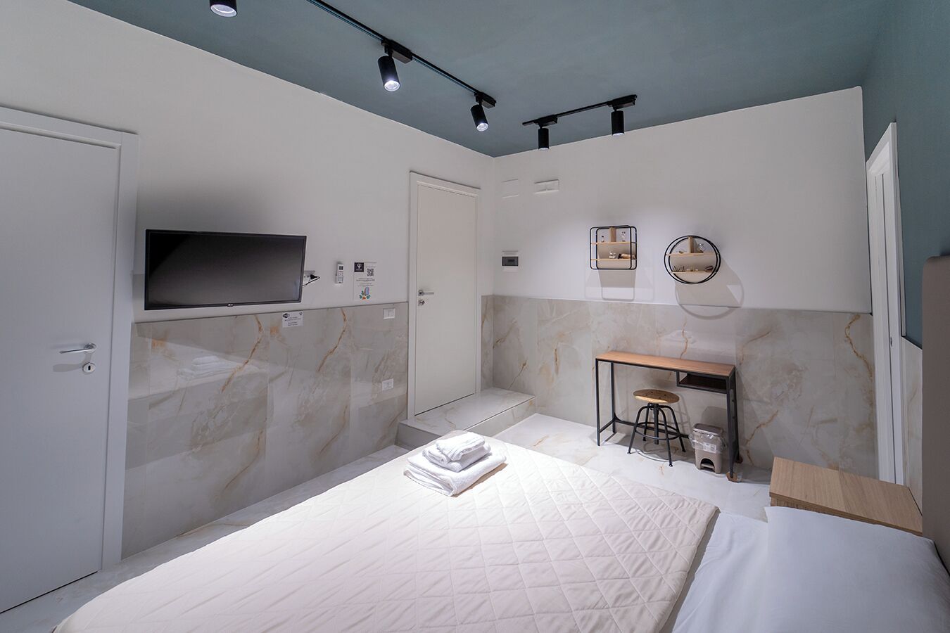 A modern bedroom with a bed, a desk, and a TV mounted on the wall.